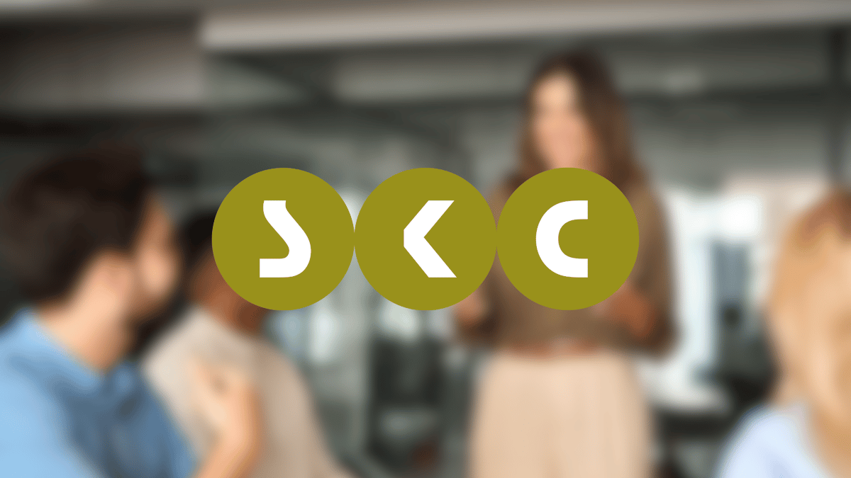 Logo von SKC Beratungsgesellschaft auf einem blurred Hintergrund in dem Personen in einem Meeting zu sehen sind.